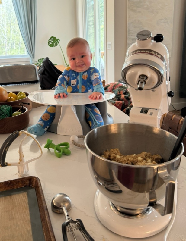 Audra's son in his seat on the kitchen counter next to a mixer full of cookie dough